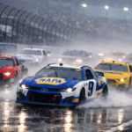 NASCAR stock cars racing at high speed on a rain‑soaked track, headlights cutting through mist as water spray rises behind them.